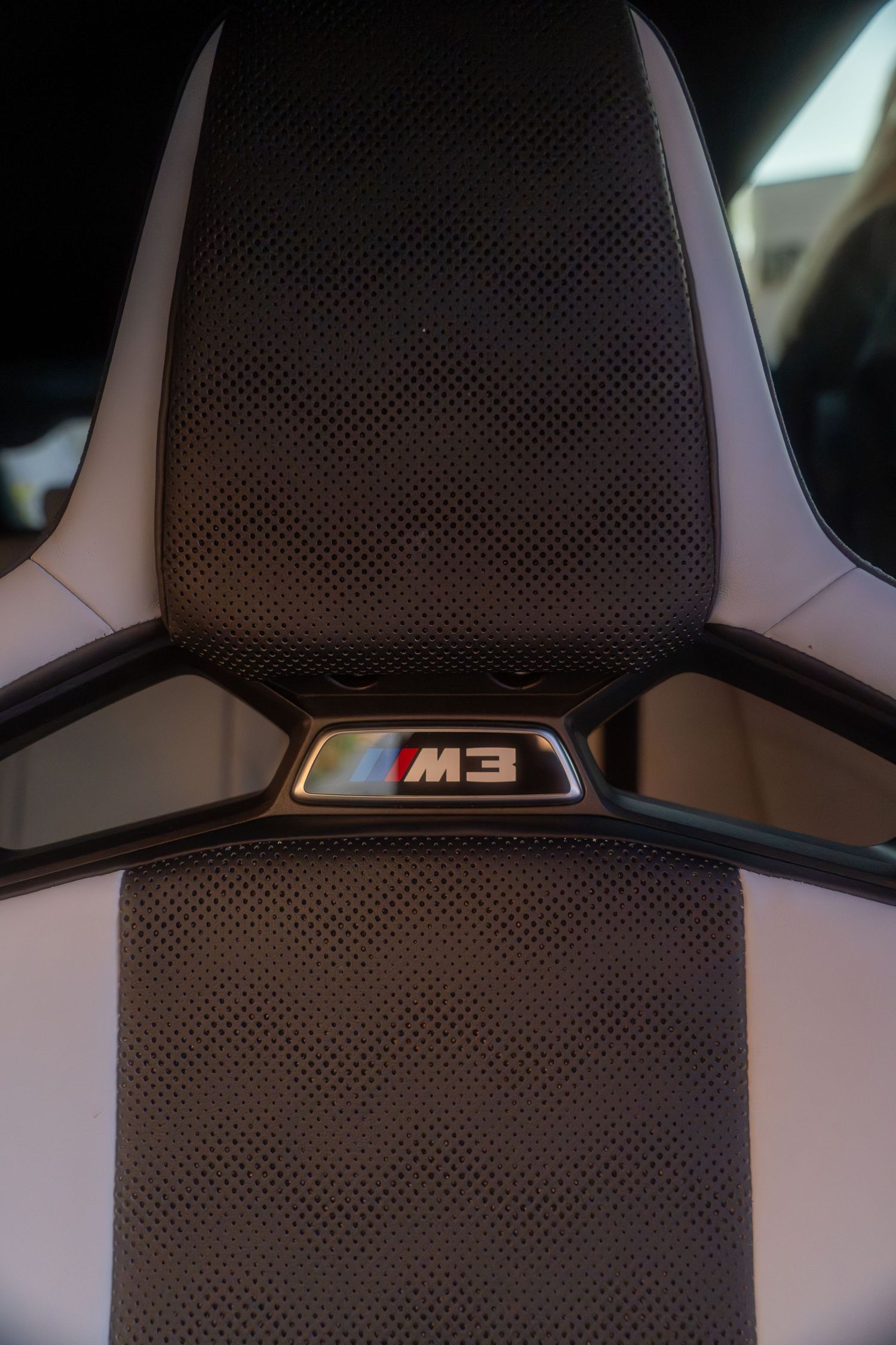 Close-up view of a BMW M3 headrest showing the embroidered M3 badge against dark perforated leather upholstery.