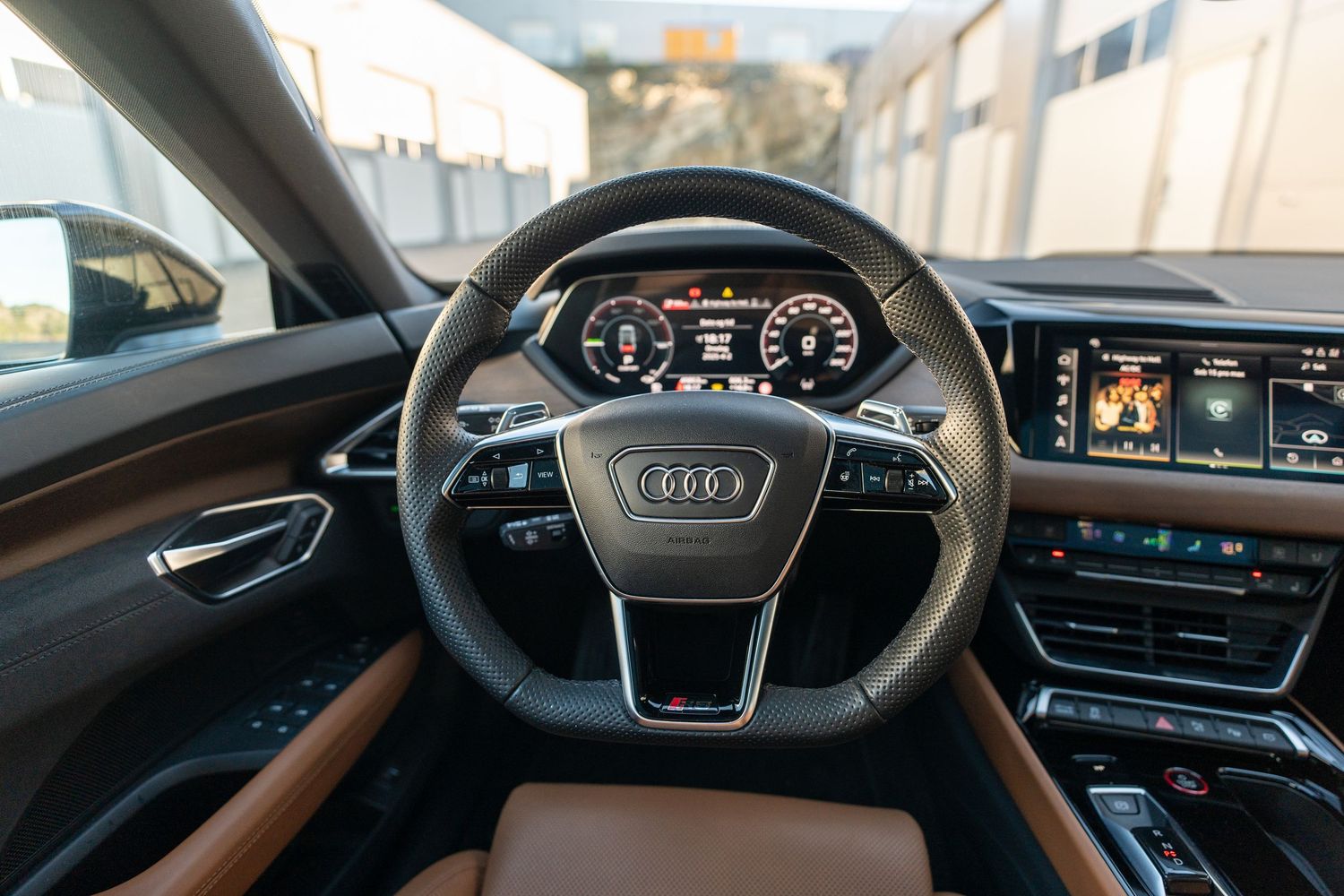 Audi steering wheel and digital instrument cluster with brown leather dashboard accents.