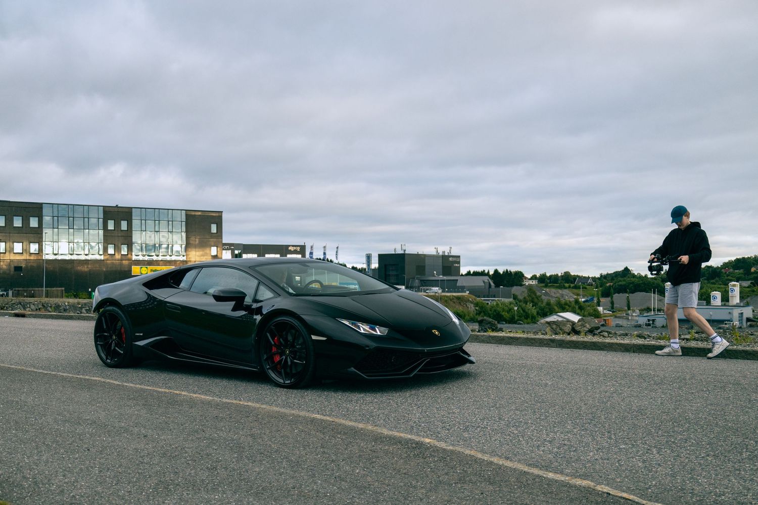Black Lamborghini Huracan parked in an empty parking lot with buildings in background.