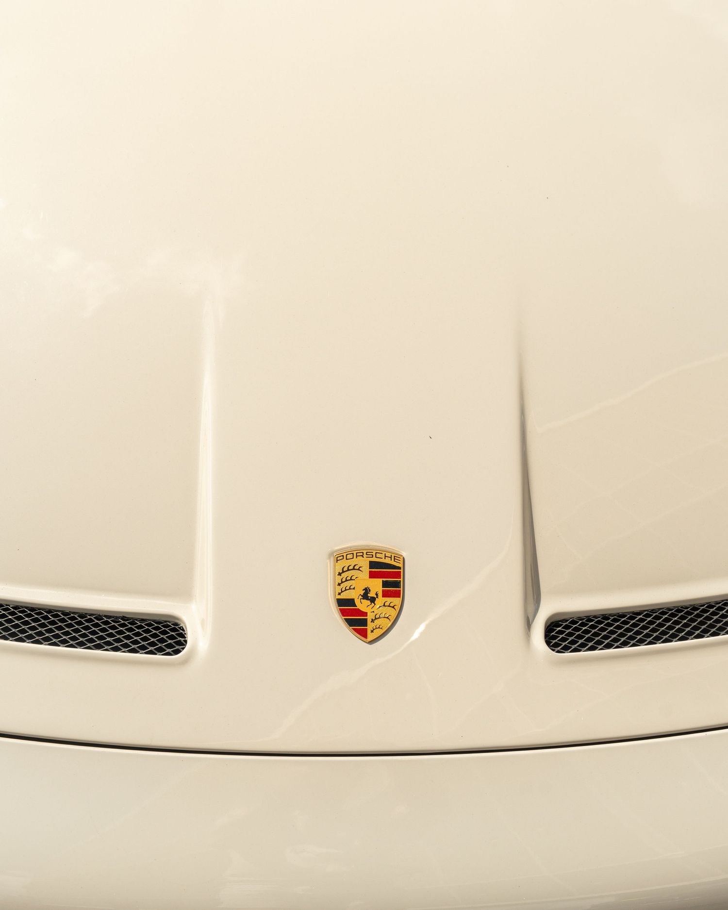 Close-up of a white Porsche hood featuring the classic Porsche emblem between mesh vents.