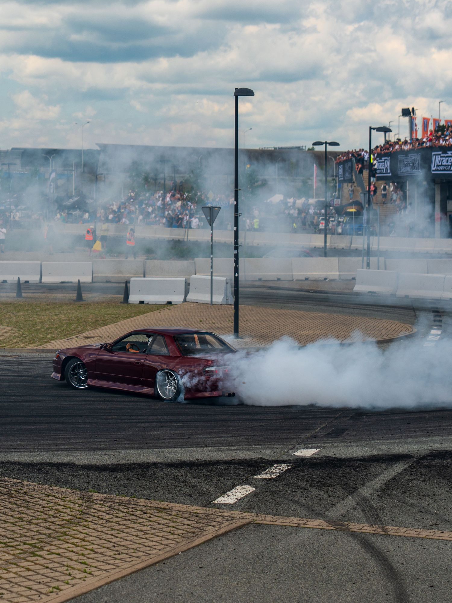 Burnout sequence showing a red modified car creating tire smoke on a paved track.