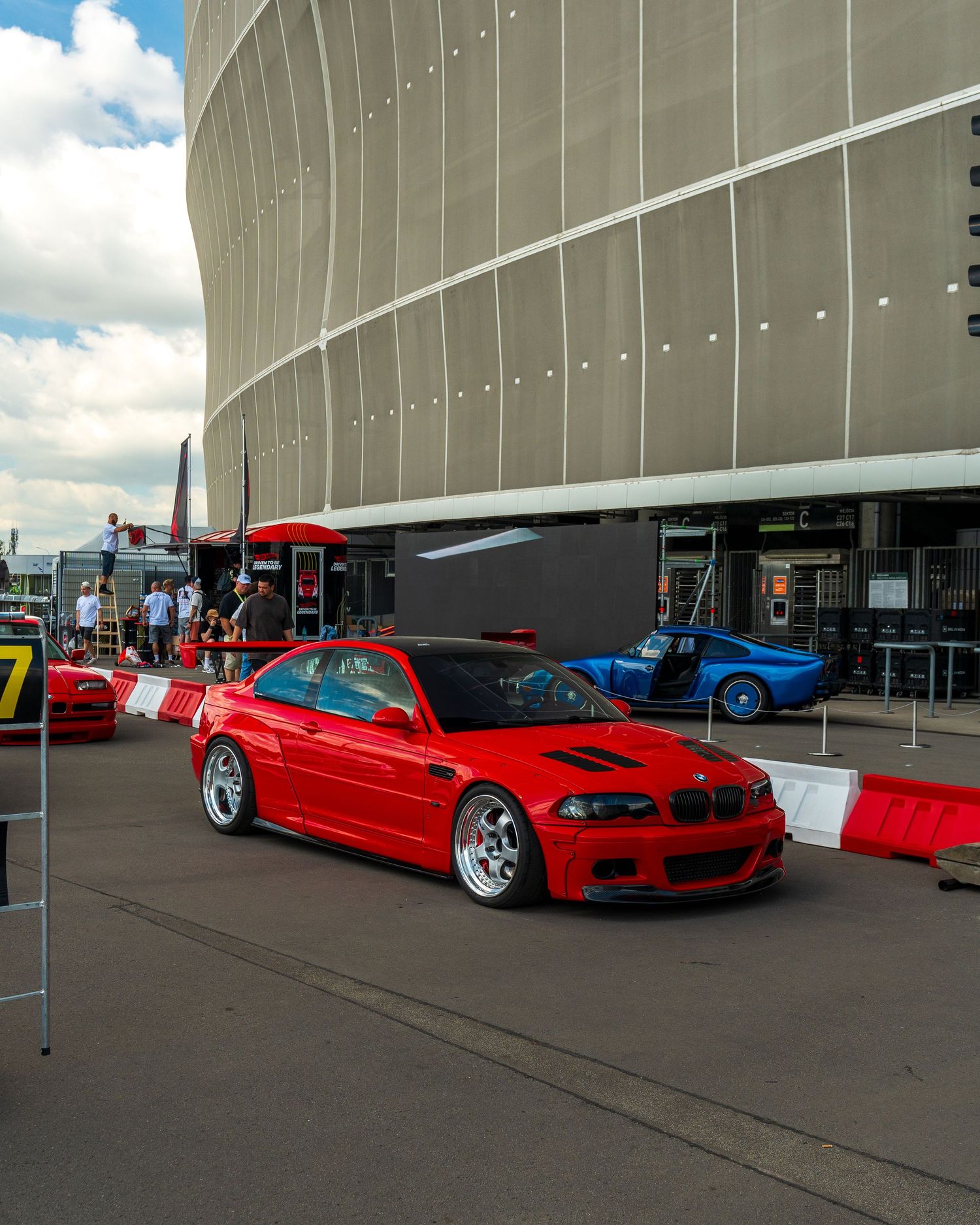 Red modified sports cars lined up against a concrete building for a car show display.
