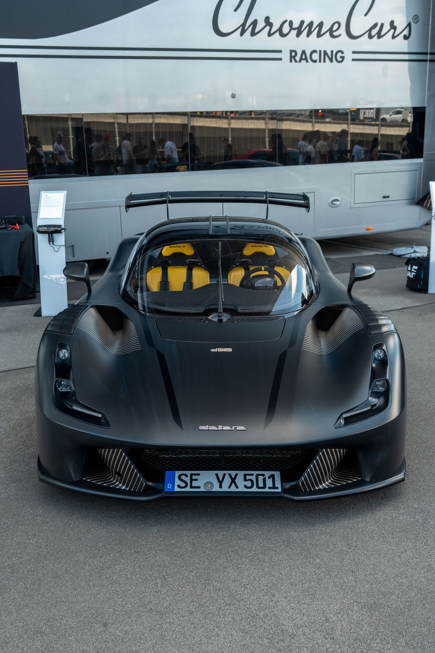 Sleek black racing car with yellow interior and aerodynamic bodywork parked in front of Chrome Cars Racing facility.