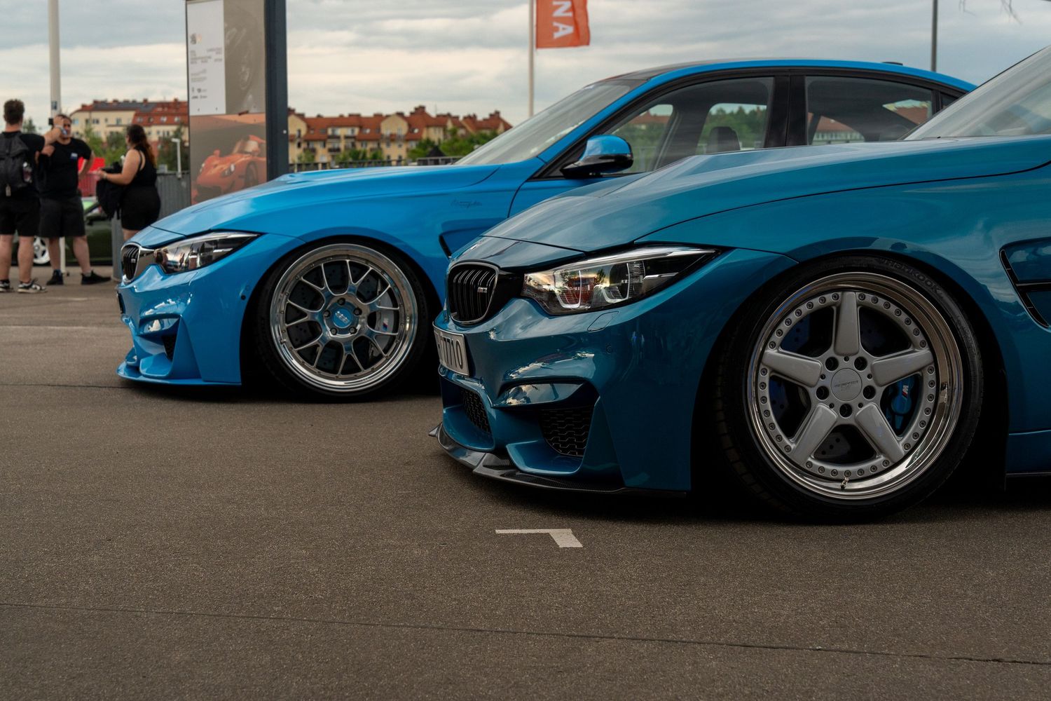 Two matching blue BMW M-series cars showing off custom wheel fitment at car show.