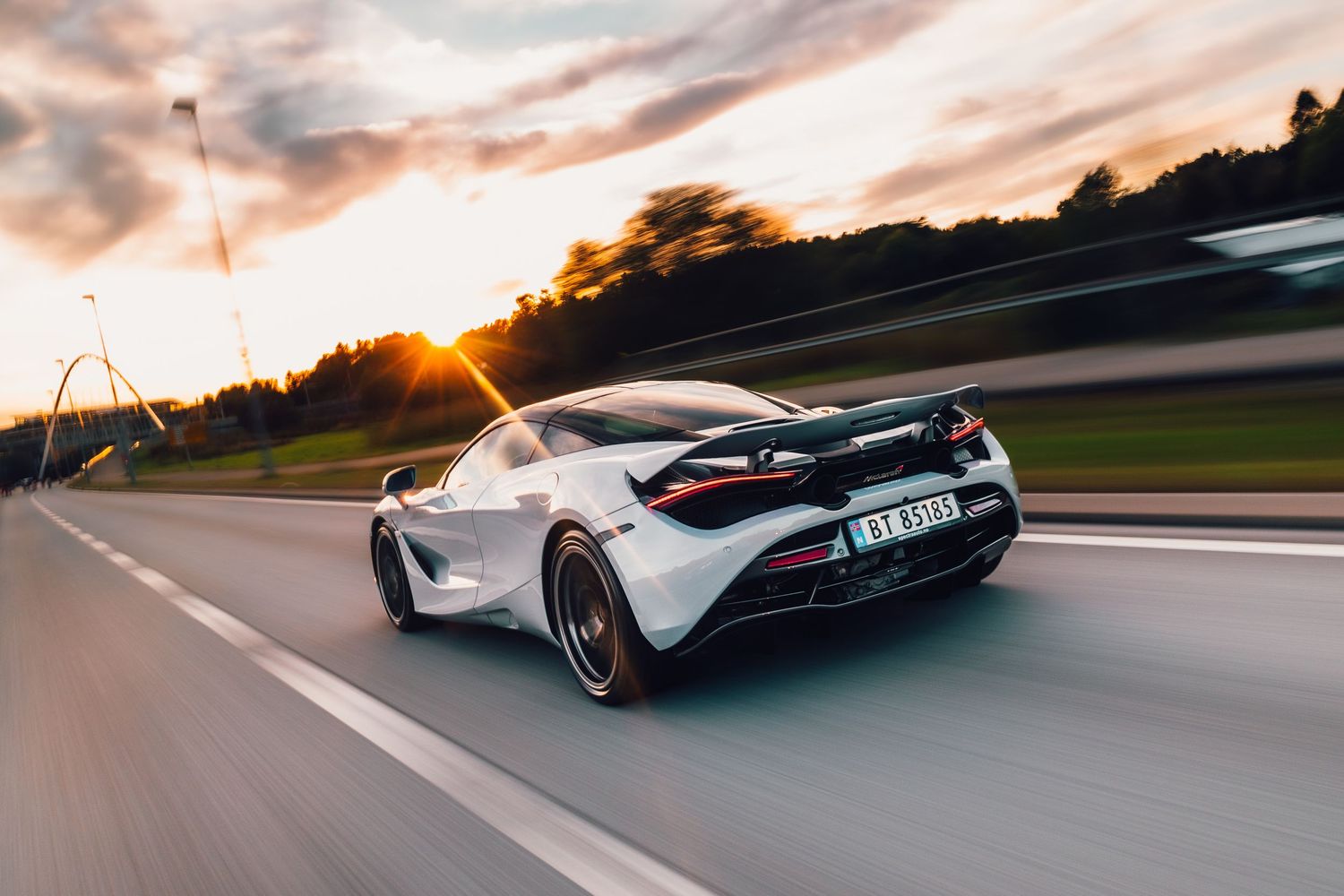White McLaren 720S sports car speeding on a highway at sunset with motion blur effect and dramatic sky.