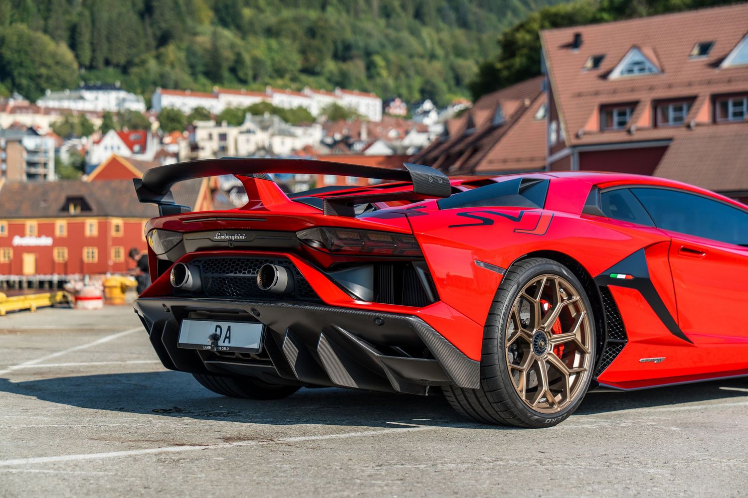 Rear view of a red Lamborghini Aventador with aggressive aerodynamics parked in a European town setting.