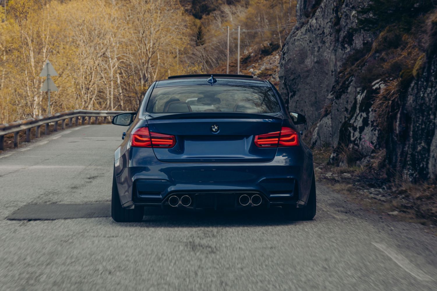 Lowered BMW M3 sports car photographed from rear on mountain road.