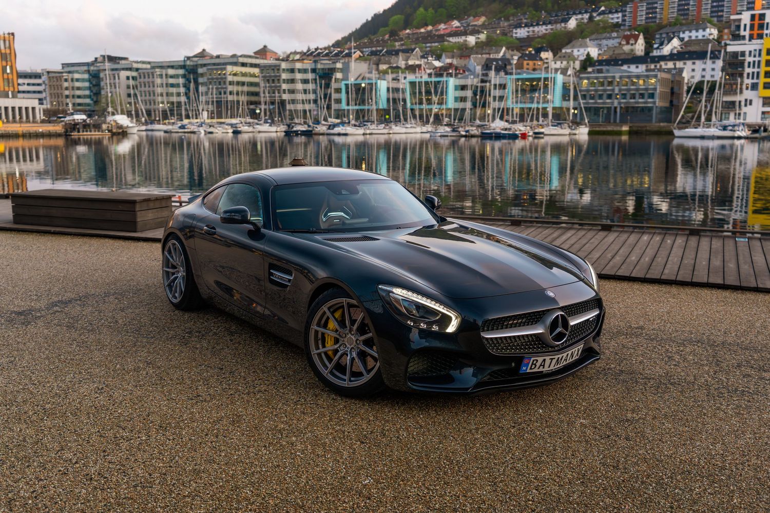 Mercedes AMG GT parked at waterfront with cityscape and harbor views.