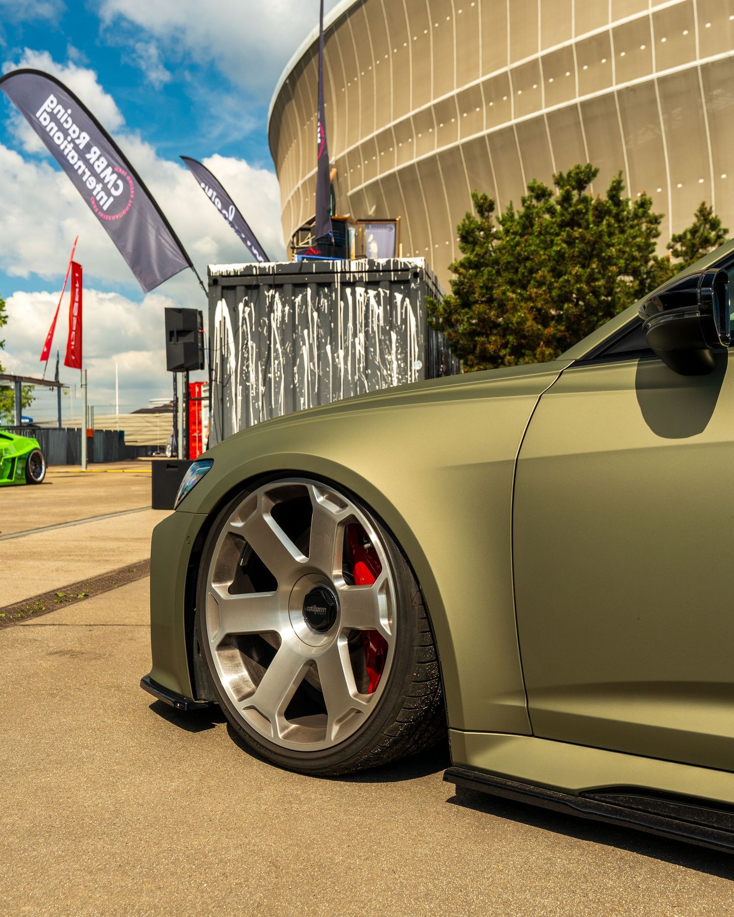 Close-up of a matte olive colored car with custom wheels and lowered suspension.