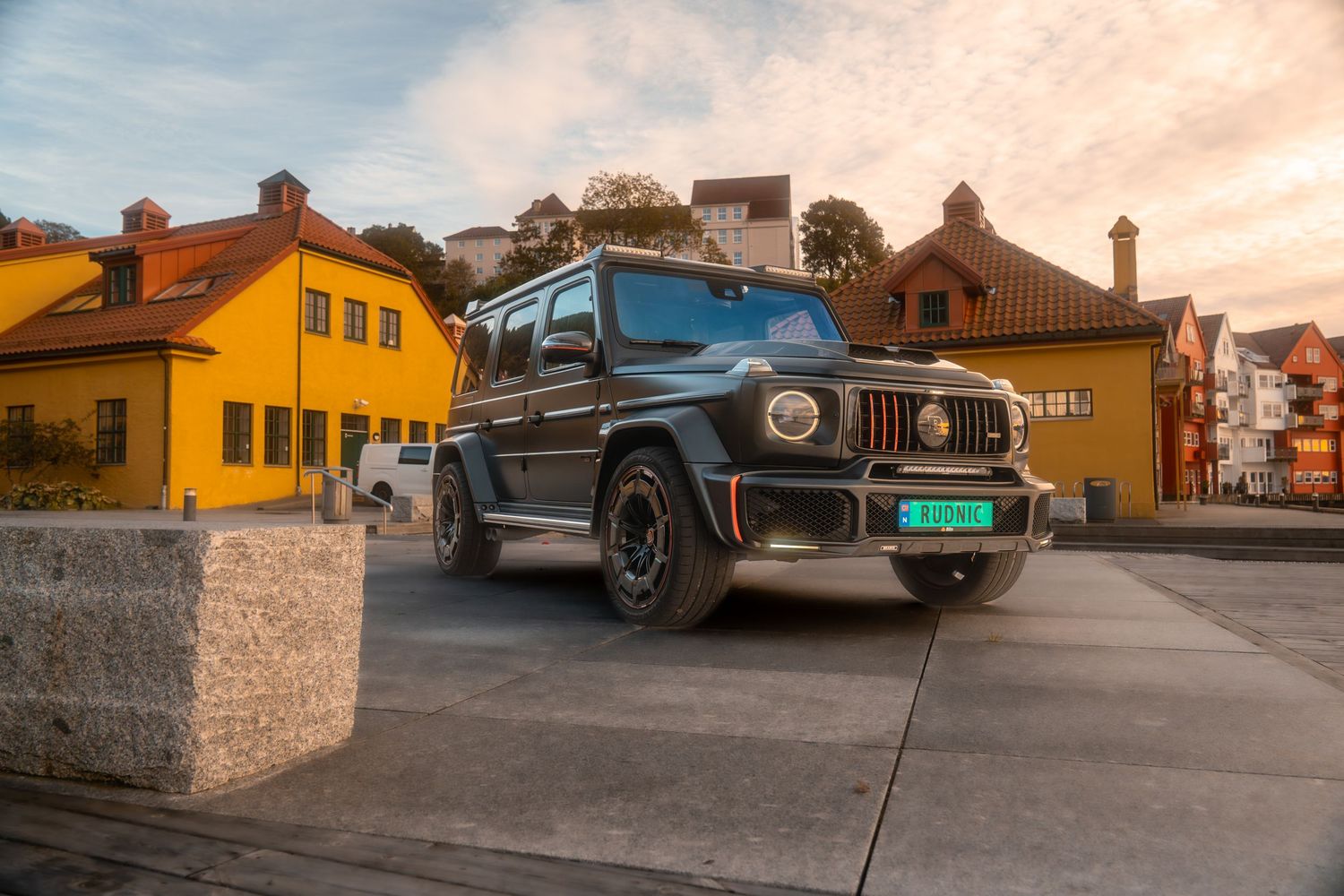 Classic vintage cars parked in a lot at sunset with yellow buildings and mountains in the background.
