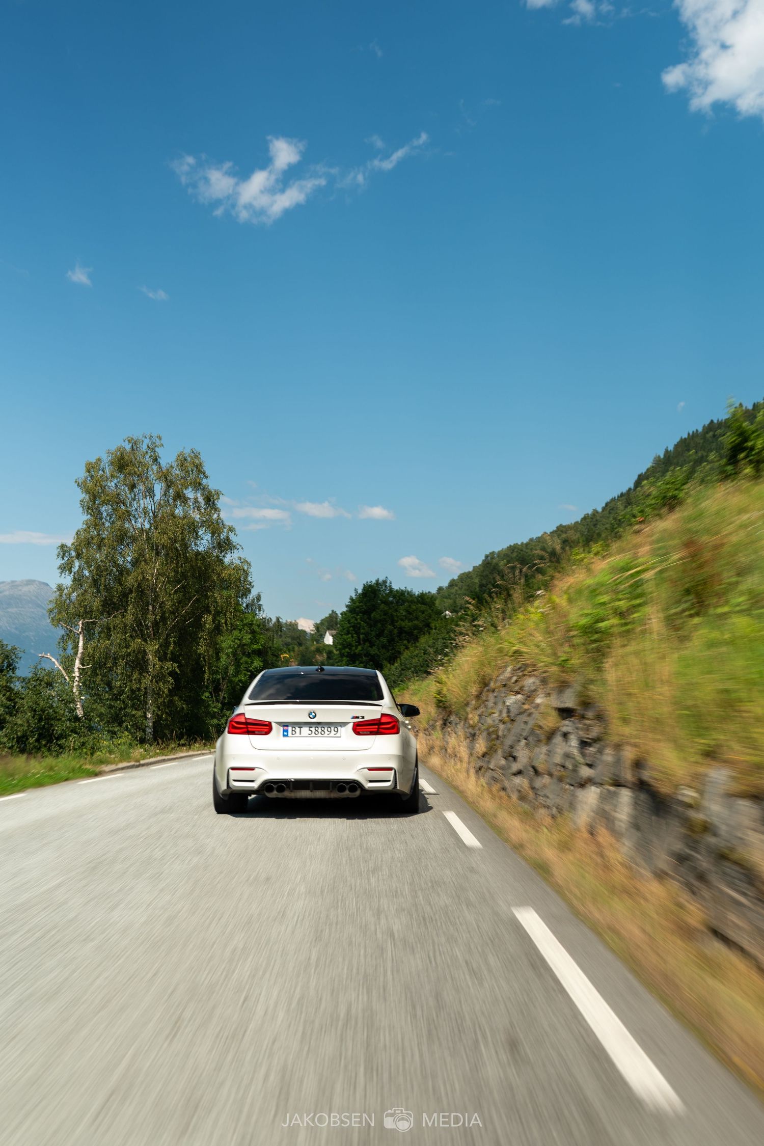 White sports car driving on winding mountain road under blue summer sky.