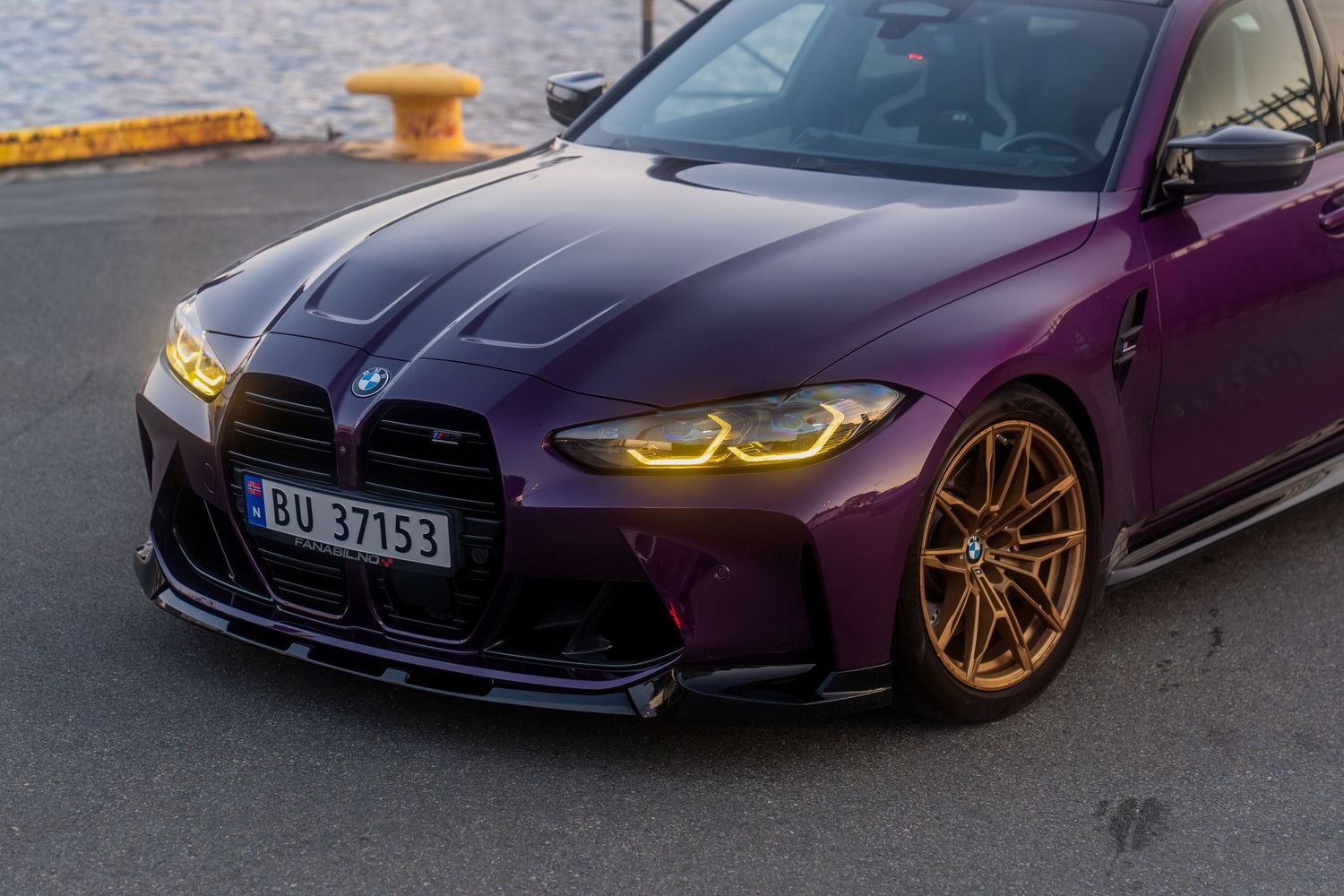 Side profile view of a customized purple BMW M4 with gold wheels against an urban backdrop.