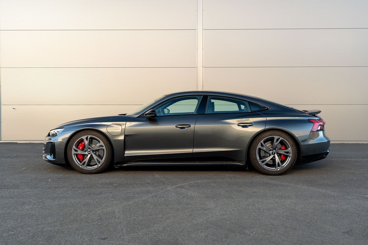 Profile shot of grey Audi RS e-tron GT with red brake calipers against industrial backdrop.