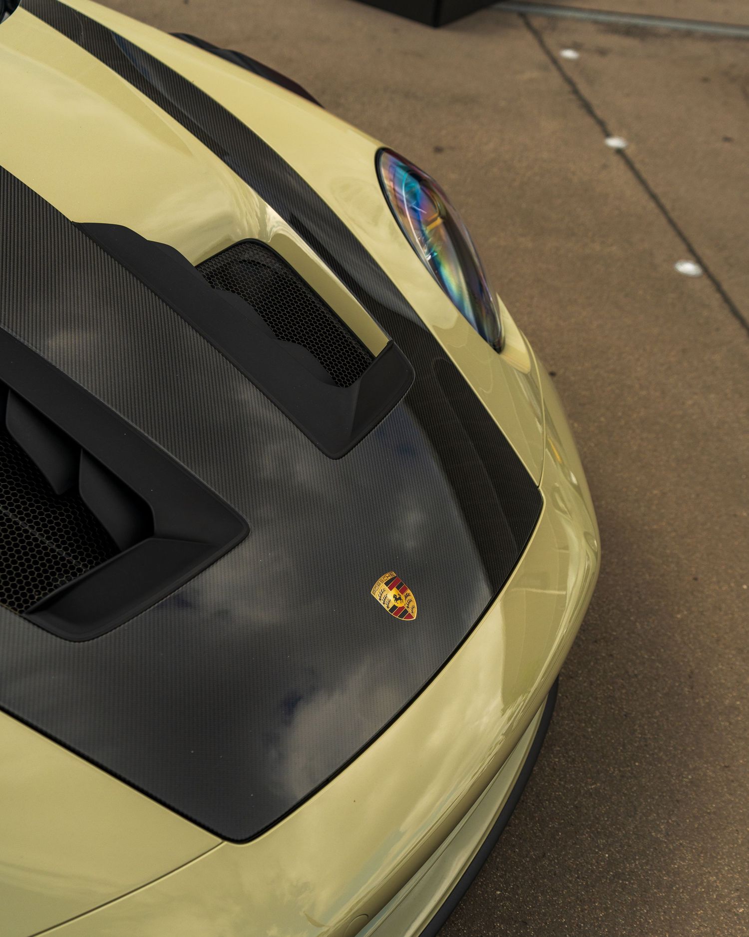 Detail shot of cream-colored Porsche hood with black accent panel and signature badge.