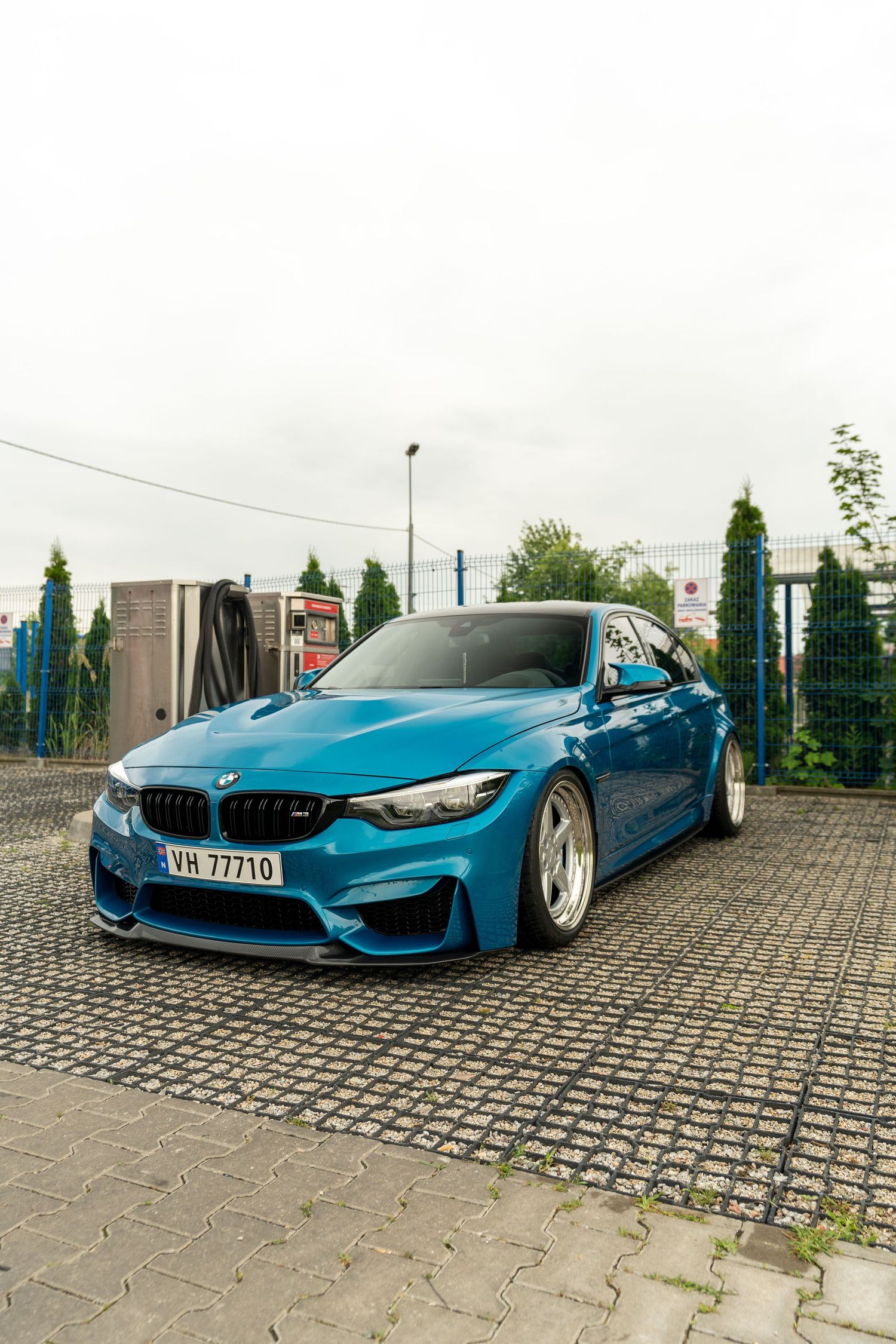 A metallic blue BMW M4 with lowered suspension and custom wheels parked on cobblestone pavement.