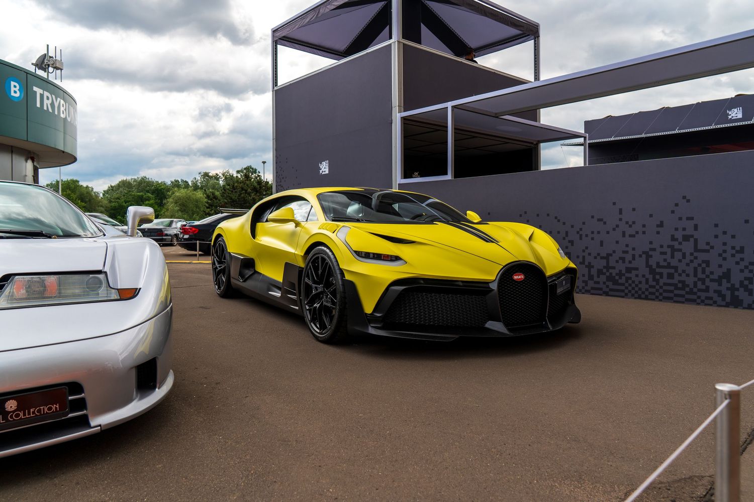 Yellow Bugatti hypercar parked at an outdoor automotive event under cloudy skies.
