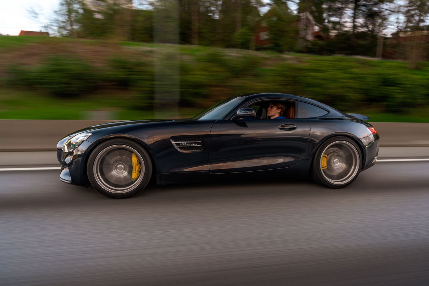 Black Mercedes AMG GT sports car in motion on a highway with motion blur and golden wheels.
