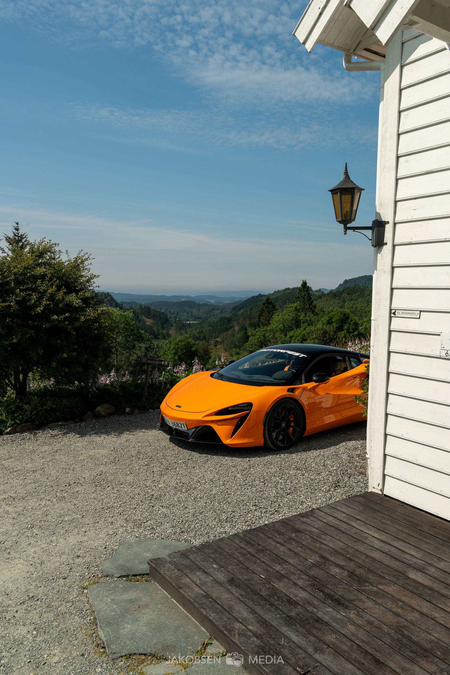 Orange McLaren supercar parked next to a white building with mountain scenery in the background.