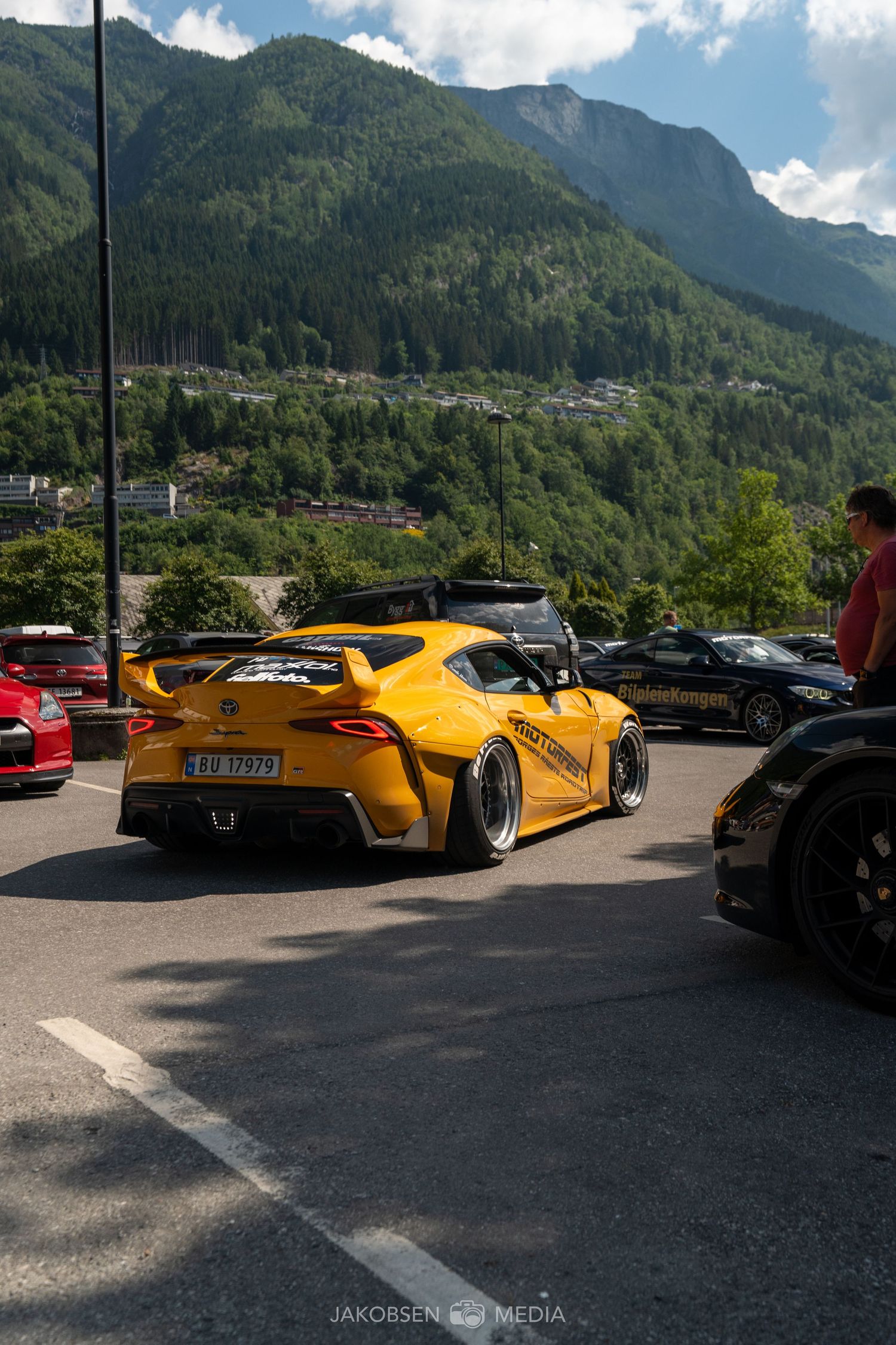 Yellow supercar parked in a mountainside lot with scenic mountain peaks and blue skies overhead.