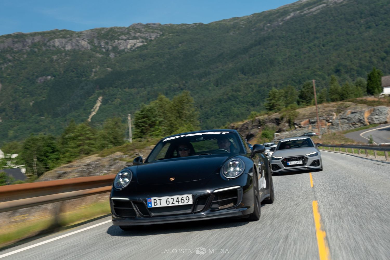 Performance vehicles driving on a scenic mountain road with stunning valley views.