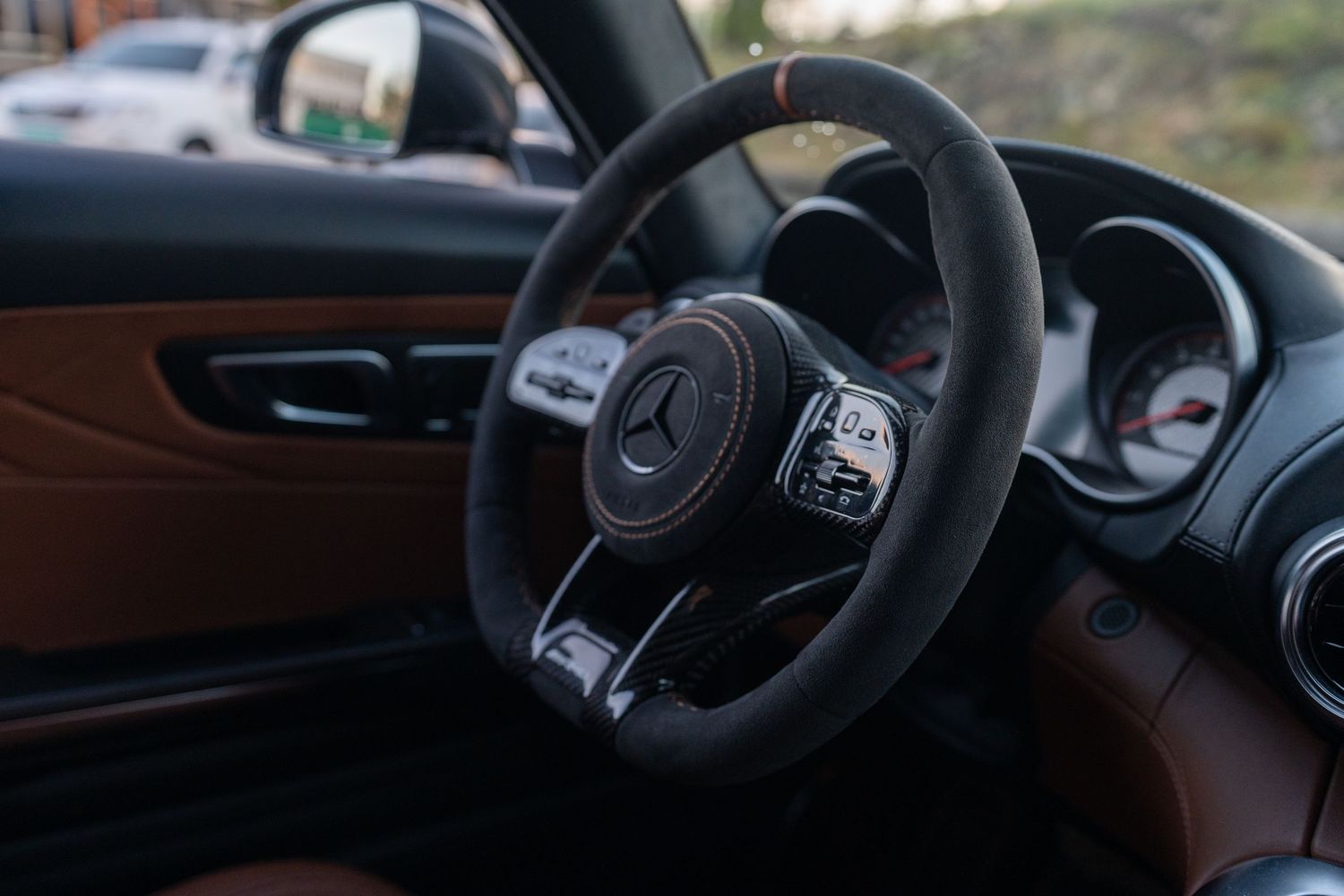 Black leather Mercedes-Benz steering wheel with mounted controls in a luxury car interior.