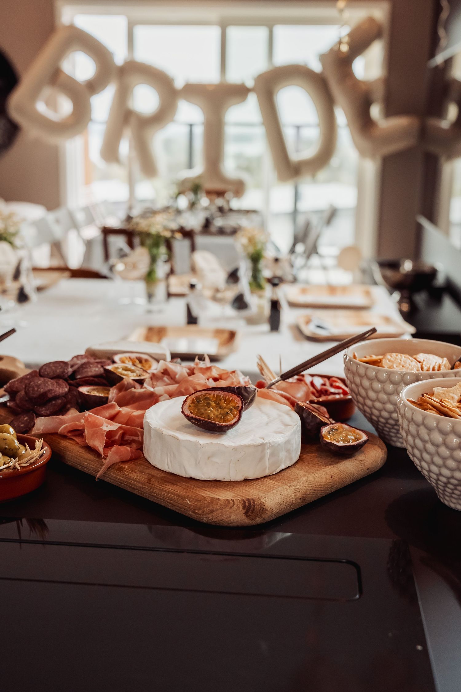 Charcuterie board with brie cheese and party snacks under birthday decorations.