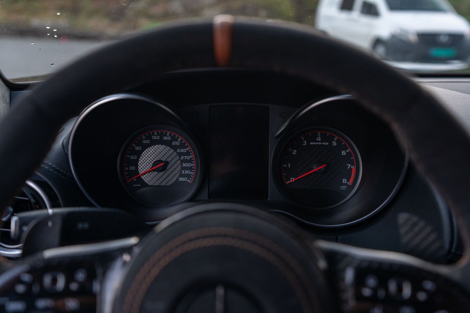 Sport gauge cluster with speedometer and tachometer behind leather steering wheel.