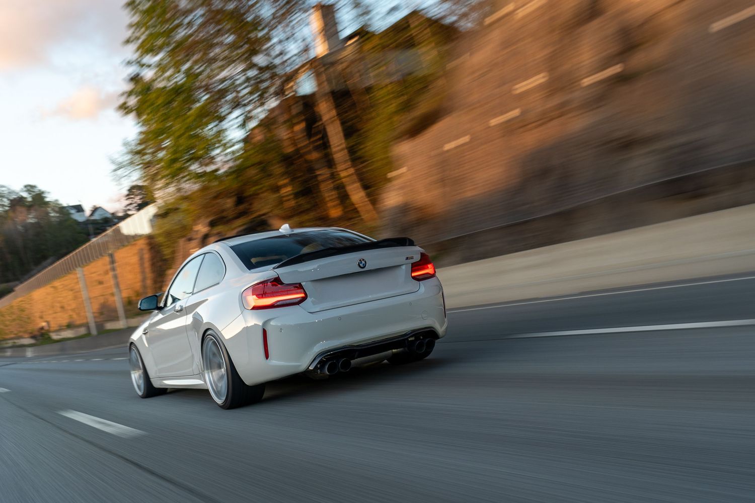 A white sports car speeds through a winding mountain road during sunset creating a dynamic motion blur effect.