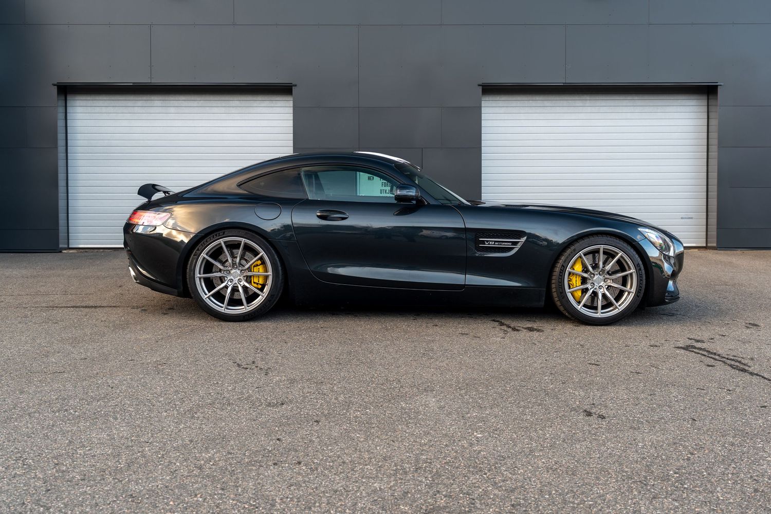 Sleek black Mercedes-AMG GT coupe with gold wheels parked in front of white garage doors.