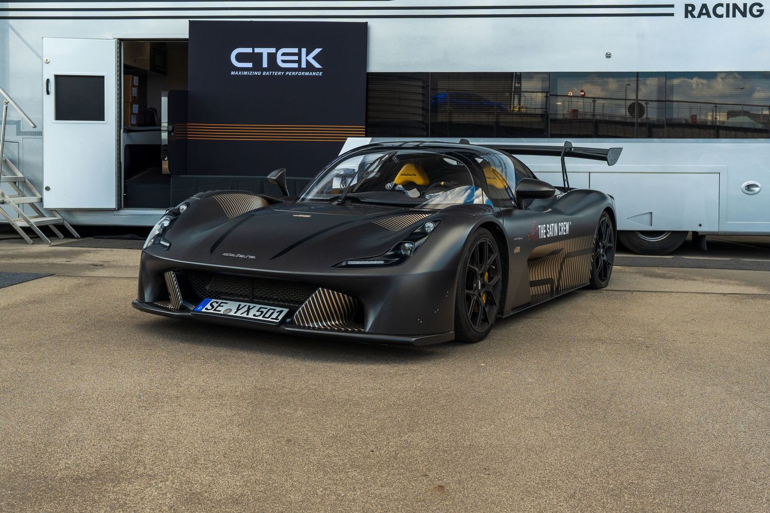 Five black and grey racing supercars lined up outdoors with sleek aerodynamic designs and large rear wings.