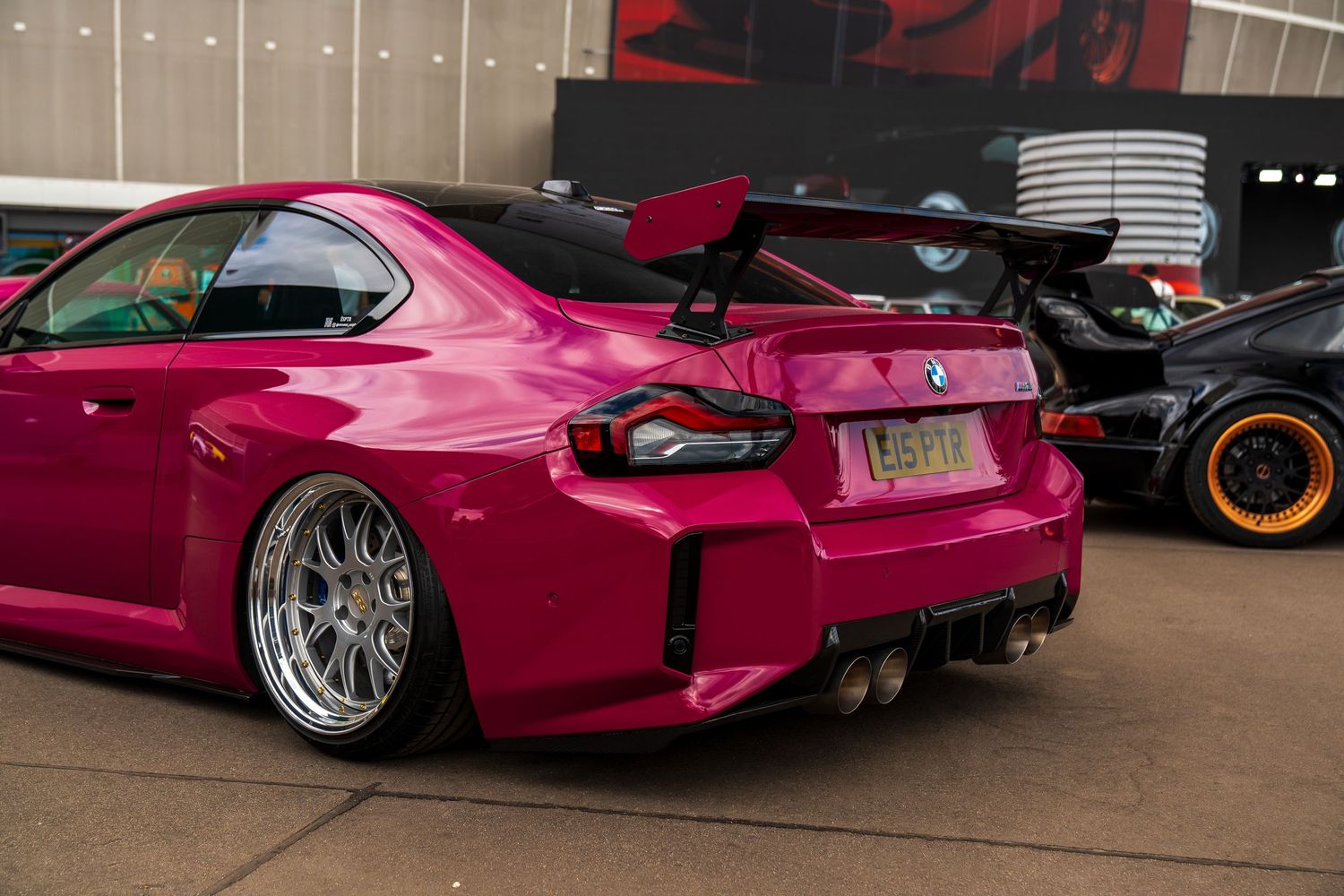 Modified pink sports car with wide chrome wheels and custom rear bodywork displayed at car show.