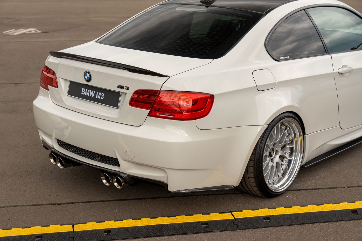 White BMW M3 rear quarter view showcasing custom aftermarket wheels and dual exhaust.