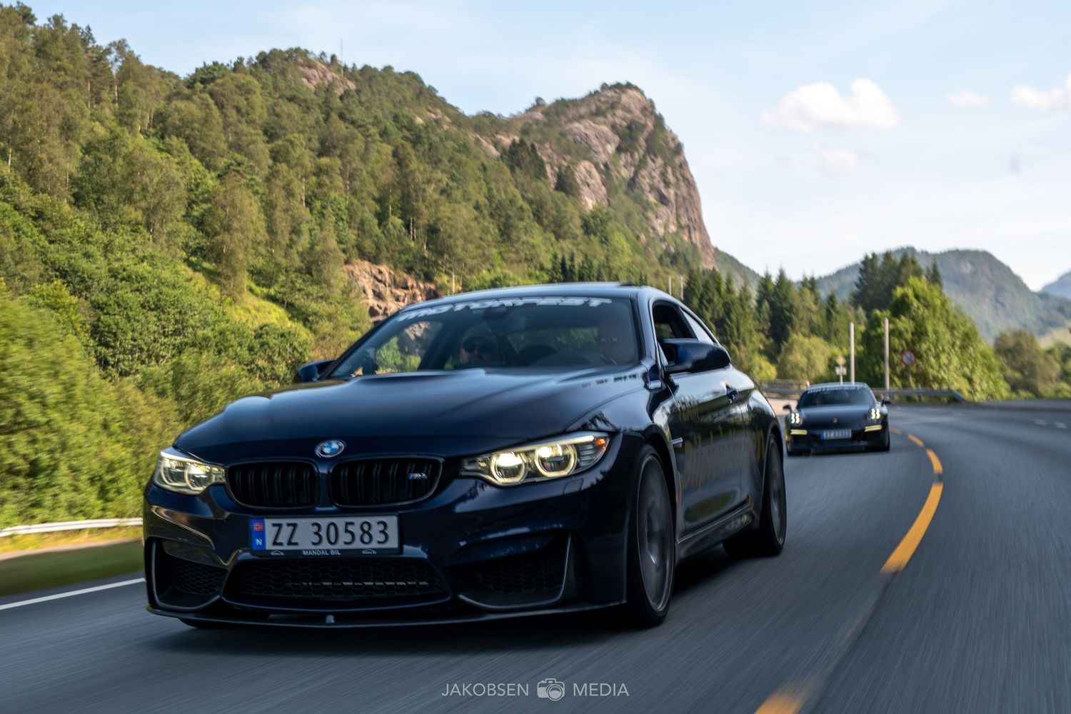 High-performance BMW vehicles cruising along a winding mountain highway with scenic forest views.