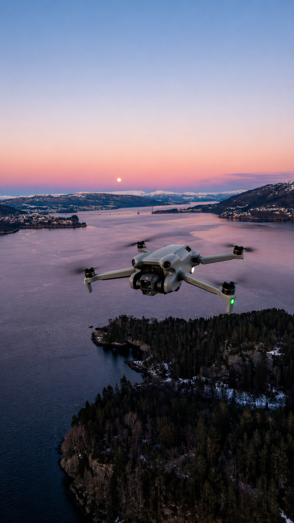 A DJI drone flies over a scenic fjord landscape at twilight, with a full moon rising over calm waters.