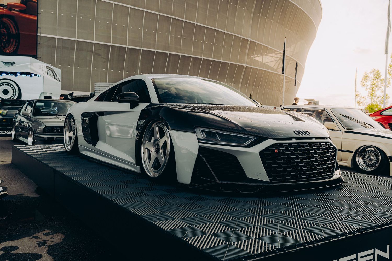 Customized white Audi R8 sports car with aggressive body kit parked at an outdoor automotive event.