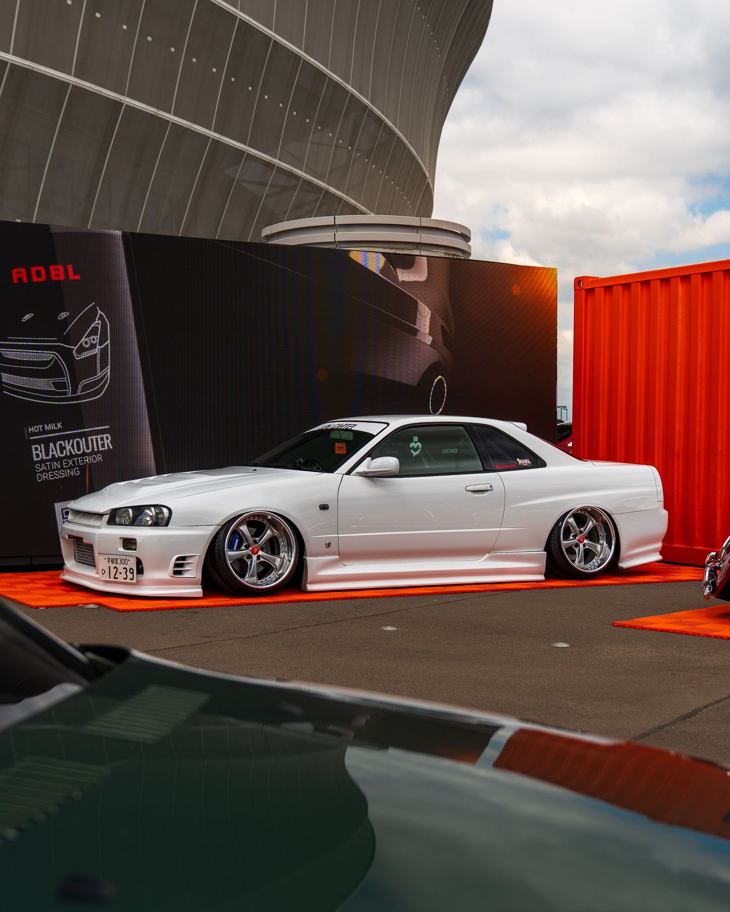 A lowered white Nissan Skyline GT-R with custom wheels displayed at an outdoor car show.