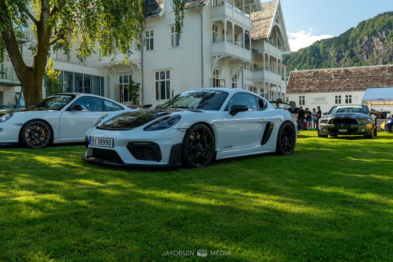High-end sports cars displayed on a manicured lawn in front of an elegant white mansion.