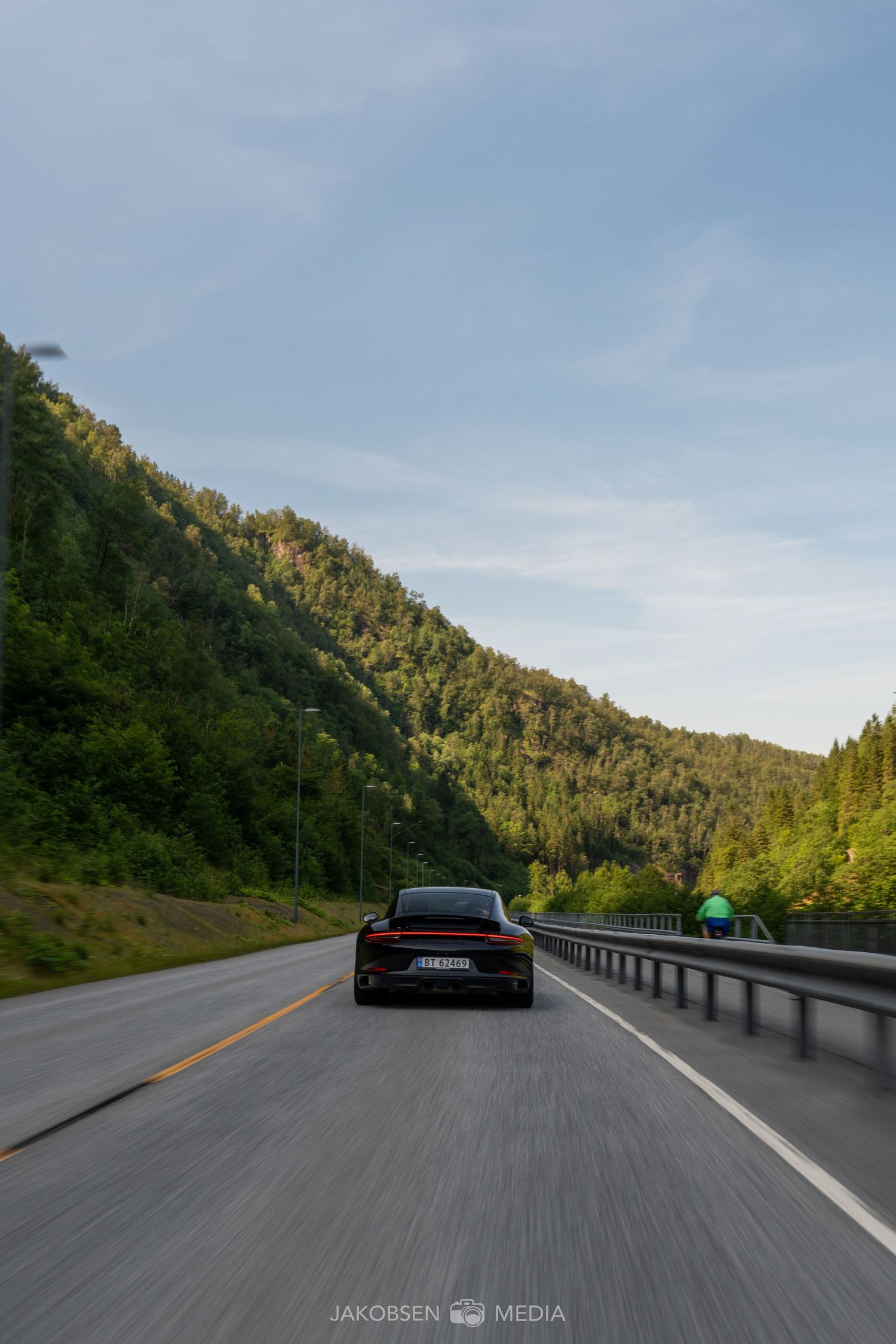 Dynamic shot of sports cars driving on a scenic mountain road with forested hills in the background.