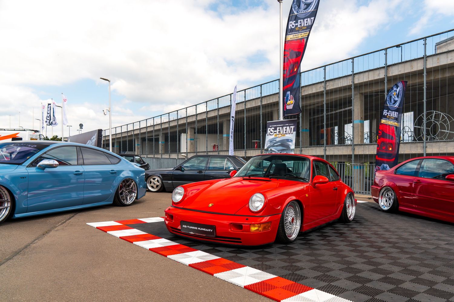 Classic red Porsche 911 on display with other modified cars at an automotive event.