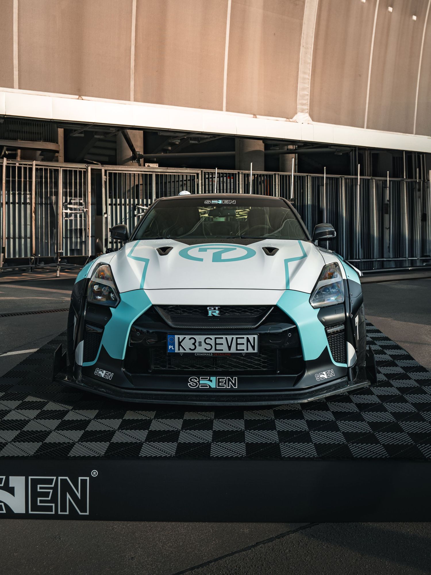 Custom turquoise sports car with sleek bodywork and unique K3 SEVEN license plate displayed in dark parking garage.