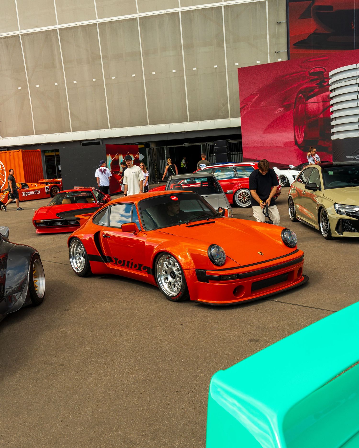 Collection of modified sports cars including orange Porsche models displayed at an indoor car show.