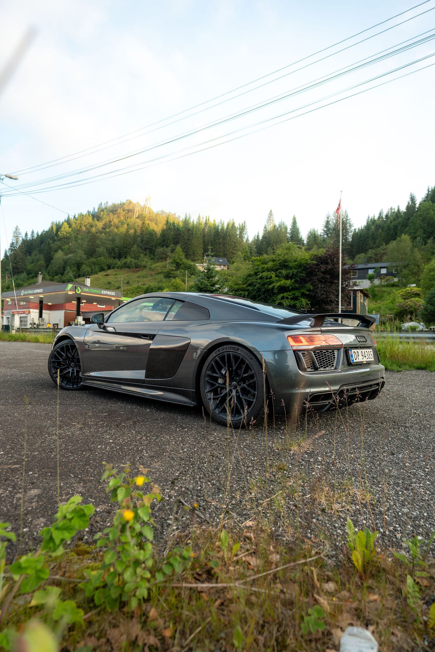 Gray supercar parked on gravel with scenic mountain landscape in background.