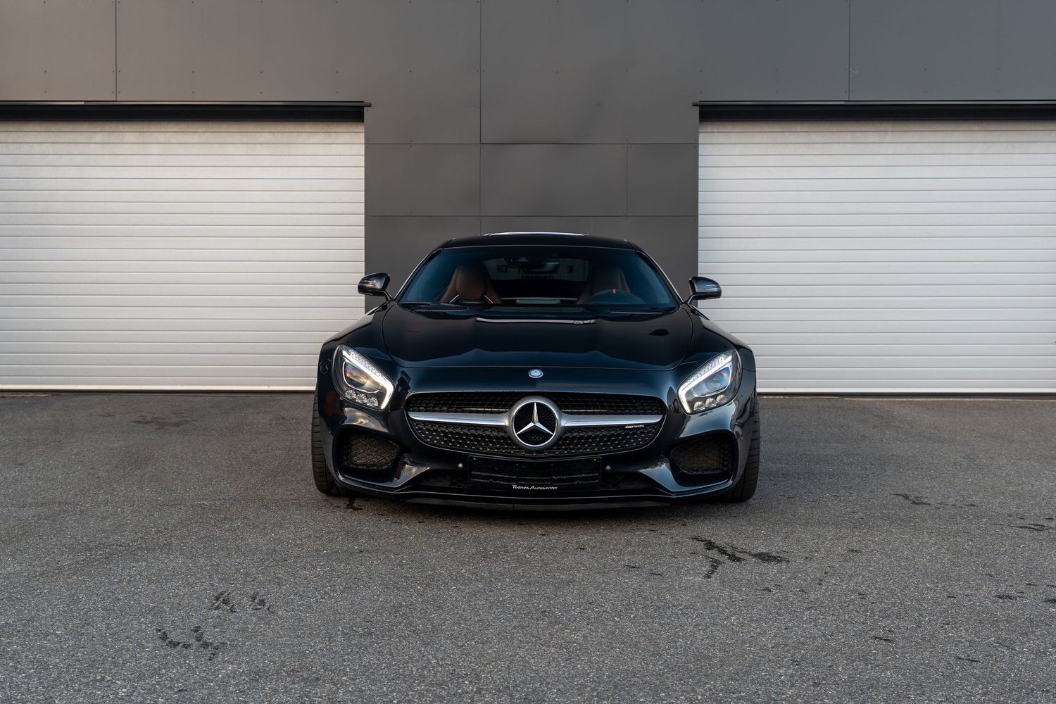 Front view of a black Mercedes-Benz AMG GT sports car against white garage doors.