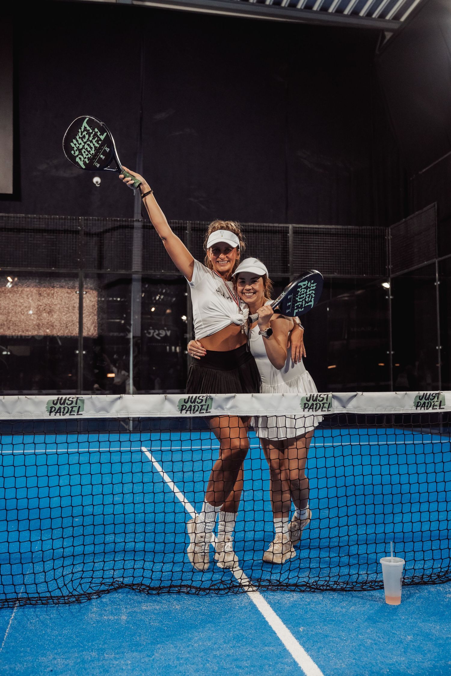Two players posing with padel rackets on blue indoor court.