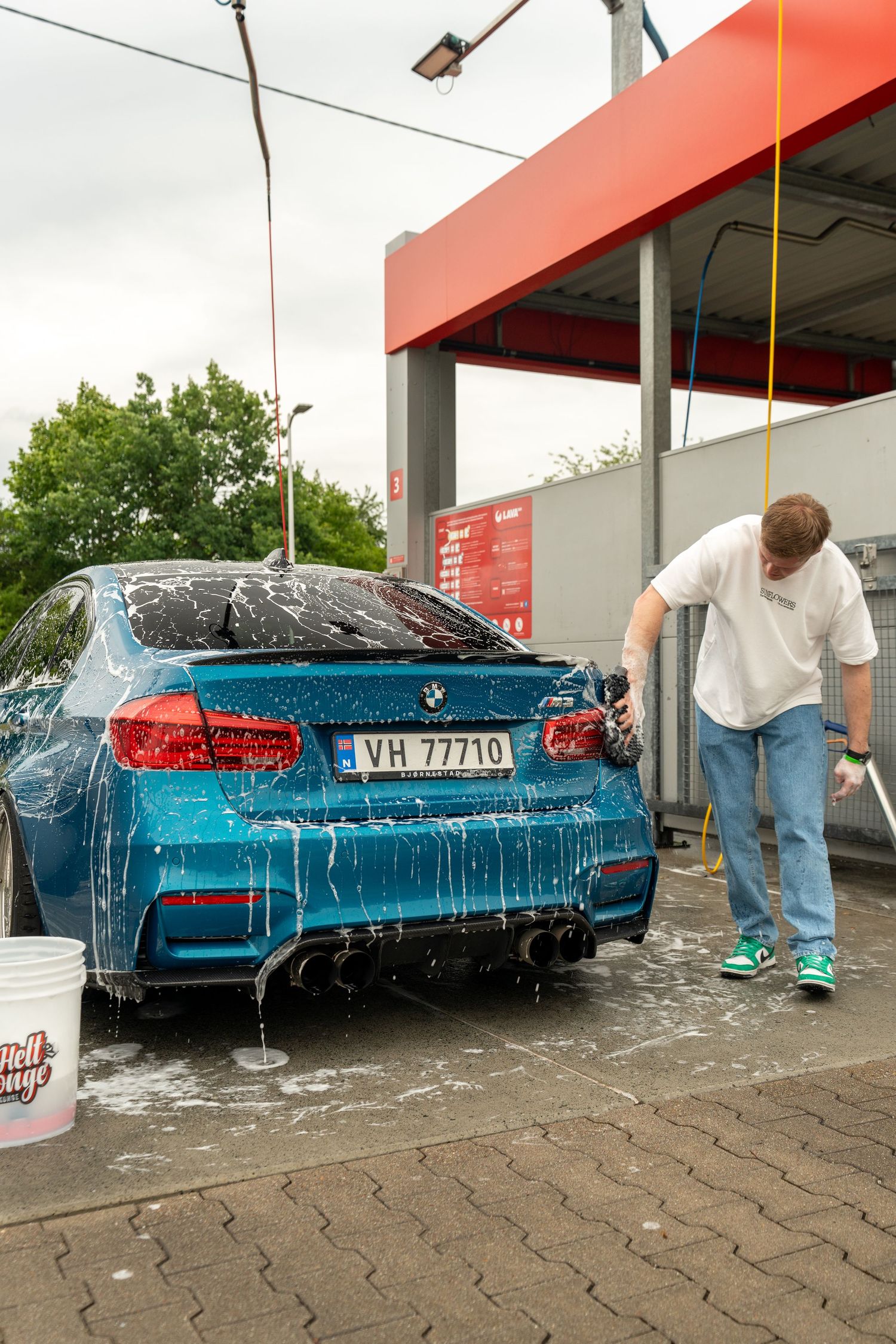 A bright blue BMW M3 being washed at a car wash station with soap suds covering the vehicle.