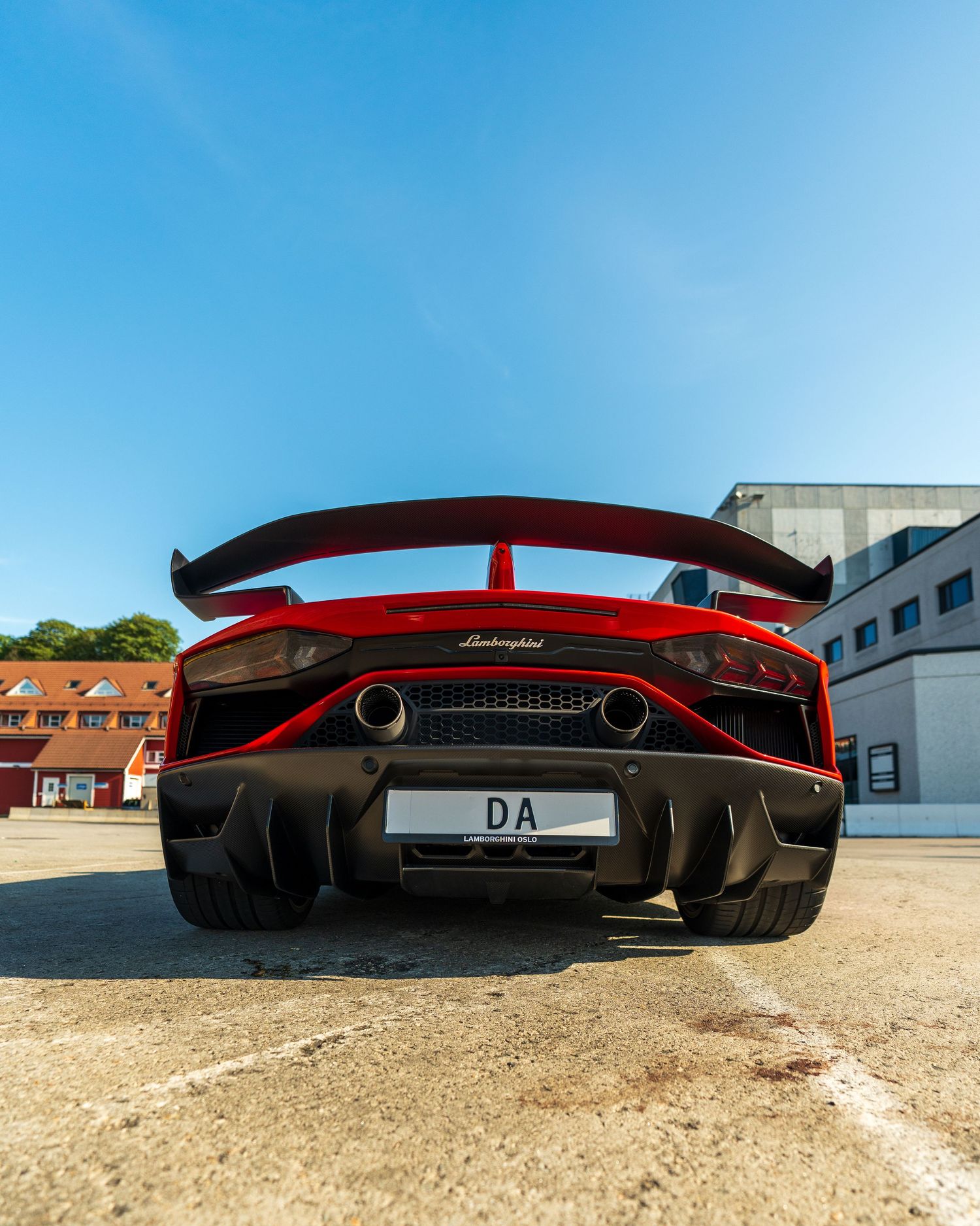 Rear view of a red supercar with large wing and aggressive diffuser against blue sky.