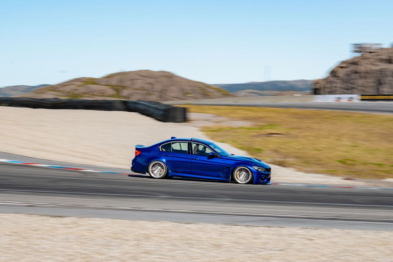 Seven consecutive motion shots of a blue BMW M3 sports car racing around a desert racetrack curve at high speed.