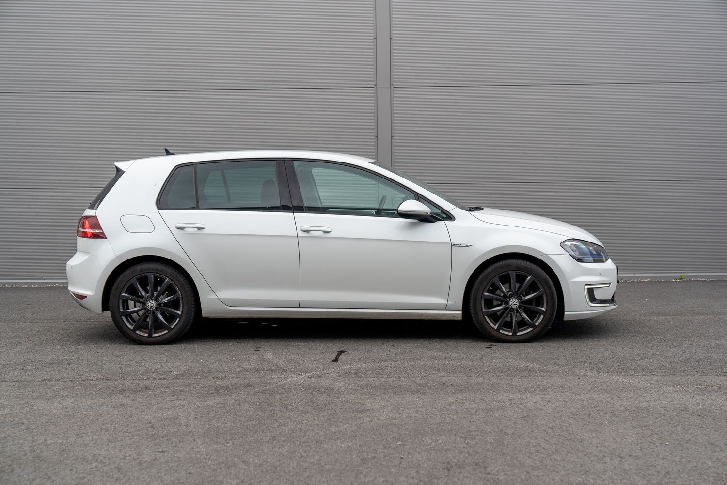 White Volkswagen Golf wagon viewed from side profile against grey industrial building.