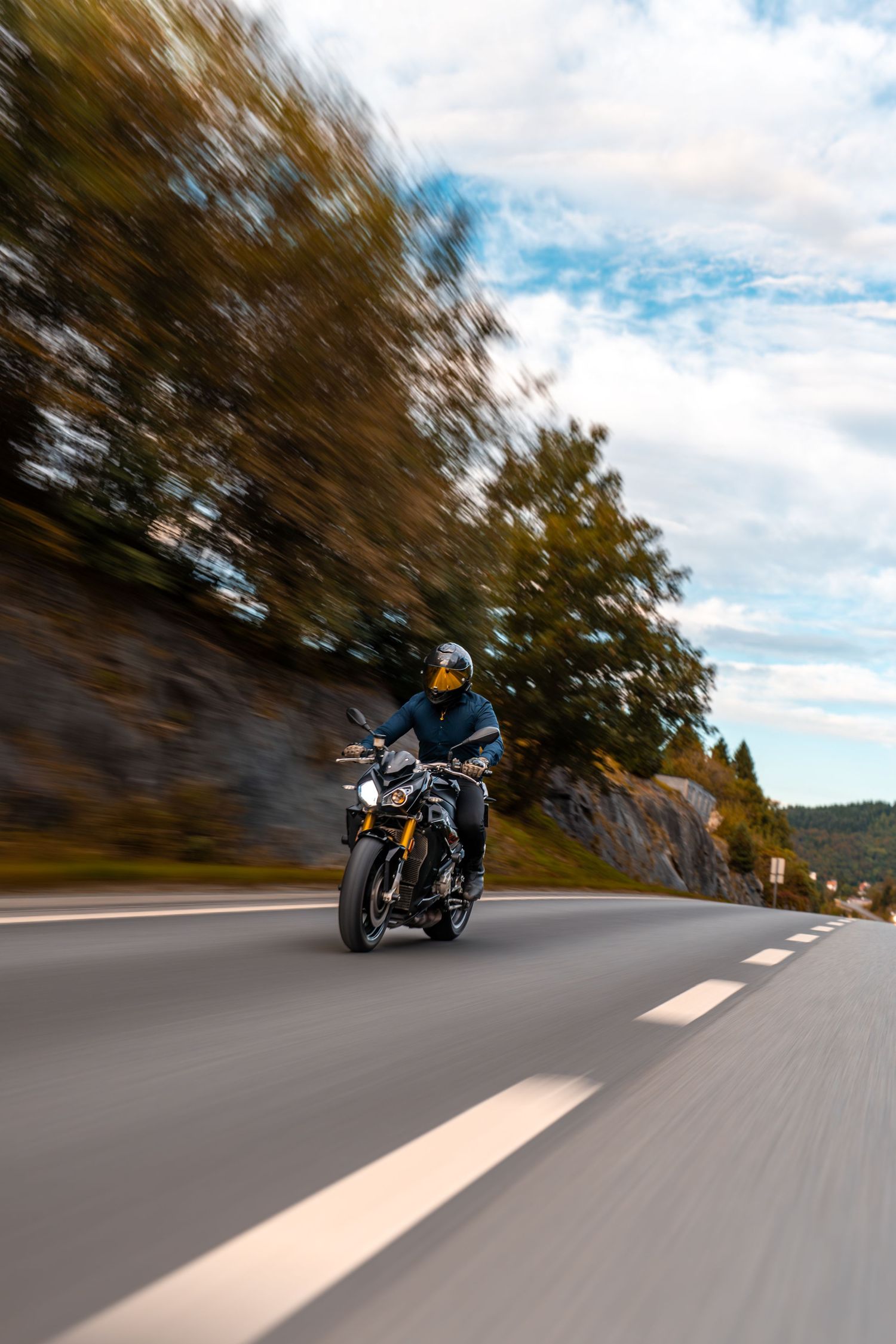 Sport motorcycle rider navigating a scenic mountain road with motion blur effect and cloudy skies.