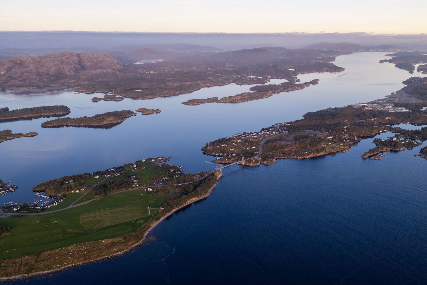 Aerial view of a scenic Scottish loch with islands, calm blue waters, and rolling hills at dusk.